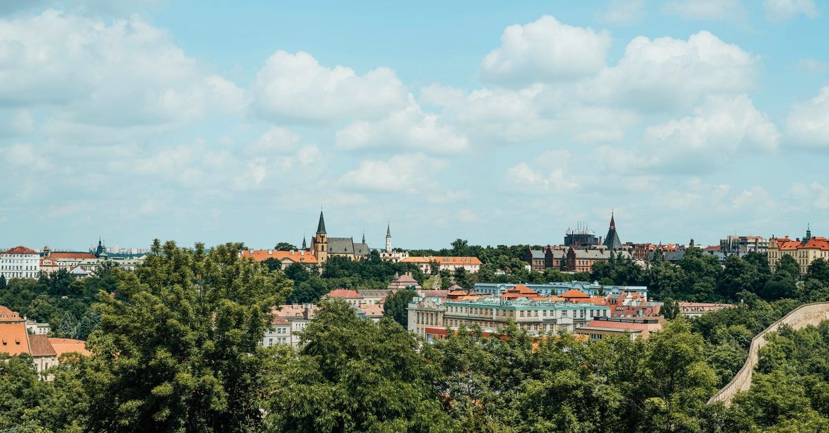 Hotel U Zvonu in Kutná Hora: A Quiet Corner Near the Main Square A panoramic view of Prague's historic cityscape with lush greenery and a clear blue sky.