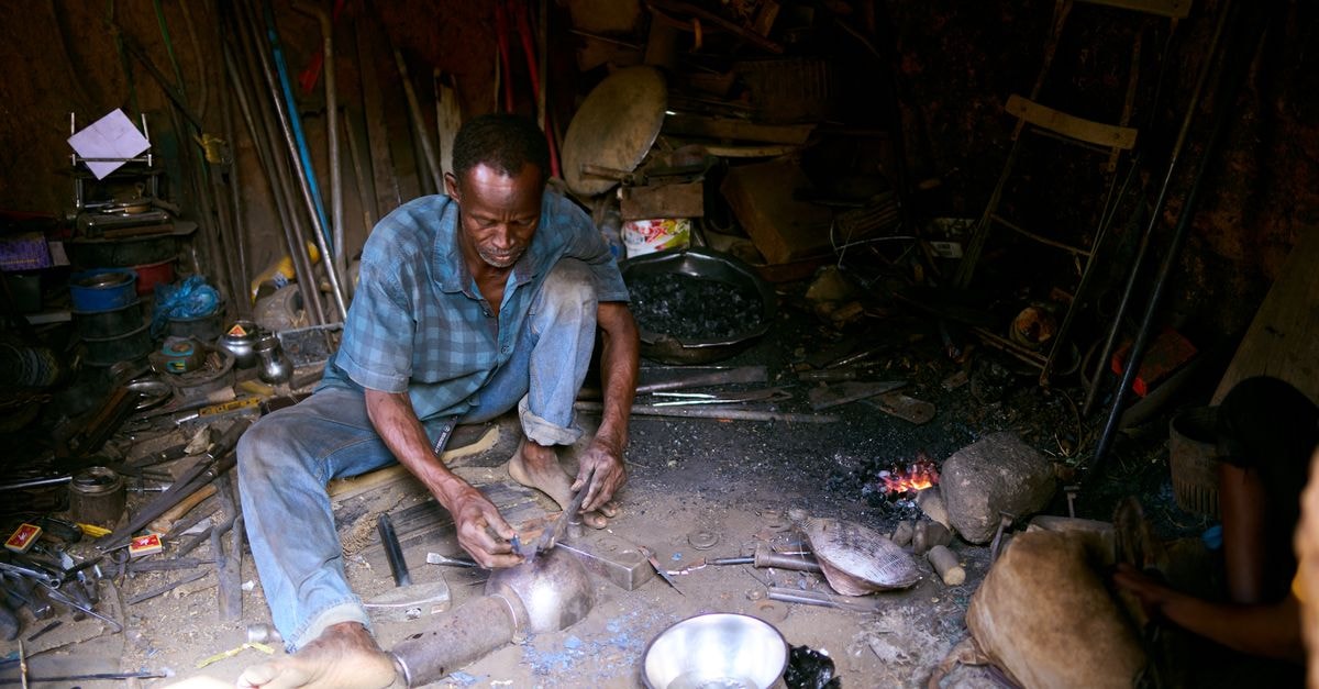 Abomey Travel Guide: Royal Palaces, Craft, and Daily Life A blacksmith shaping metal with tools in a dimly lit, rustic workshop.