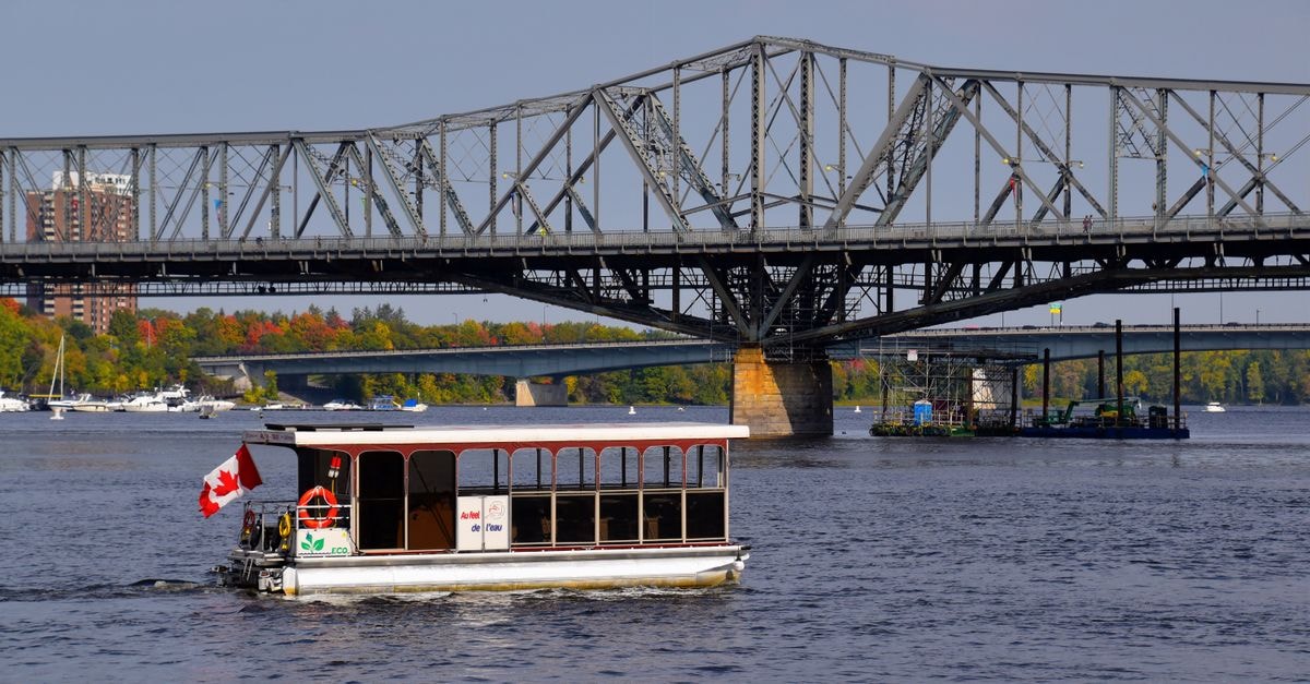 Fredericton Travel Guide: Planning Tips, Costs and Things to Do Ferry crossing Ottawa River by Alexandra Bridge with Canadian flag.