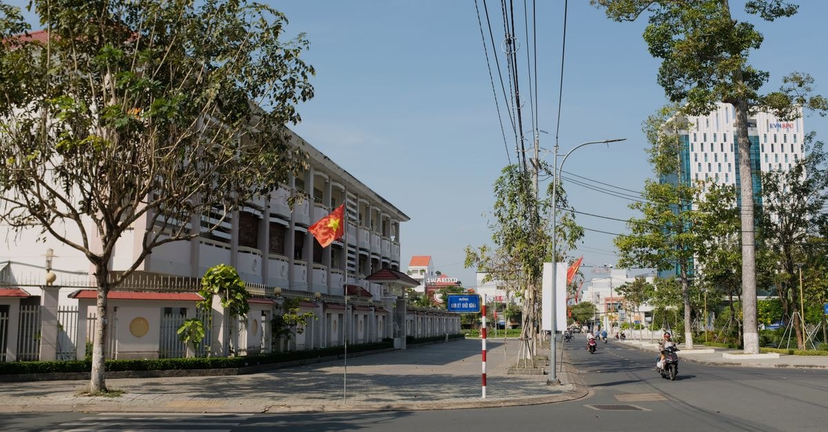 Green Homestay Bến Tre: Family Rooms, Pool and Free Bicycles in Bến Tre Street view of Bến Tre, Vietnam, with a Vietnamese flag and blue sky.