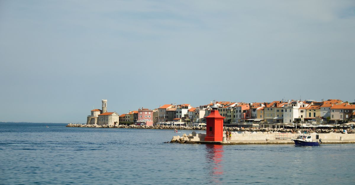 Piran Travel Guide: What to Know Before Visiting in July 2026 Picturesque view of Piran harbor in Slovenia with colorful buildings and a vibrant red lighthouse.