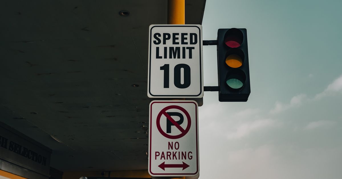 US regulators move on EV door safety rules as China's oversized EVs strain road funding Close-up of a speed limit sign and traffic lights at an intersection under a cloudy sky.