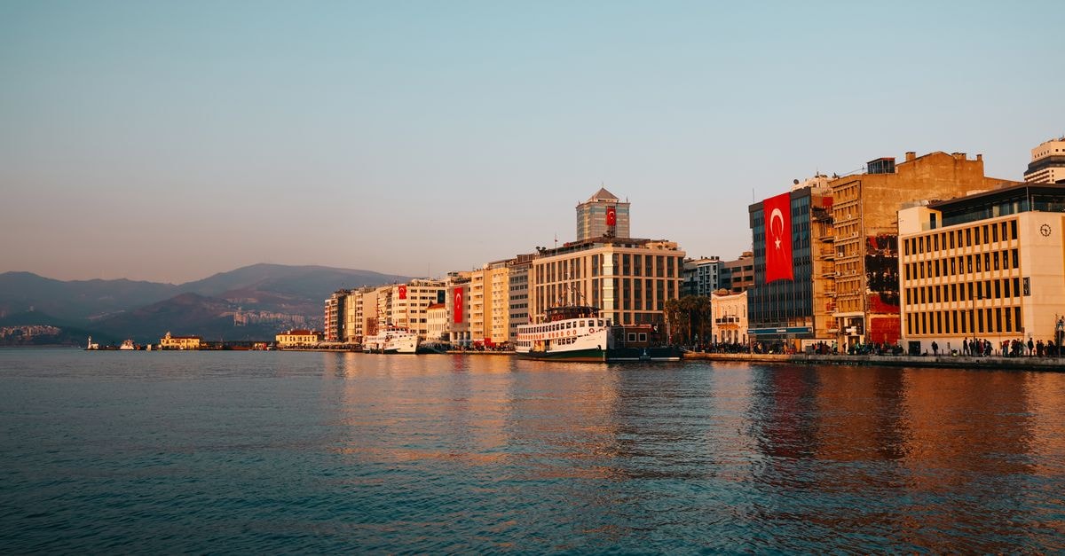 Konak travel guide: a waterfront corner of İzmir to wander slowly Scenic waterfront view of Izmir with Turkish flags at sunset, capturing city landmarks.