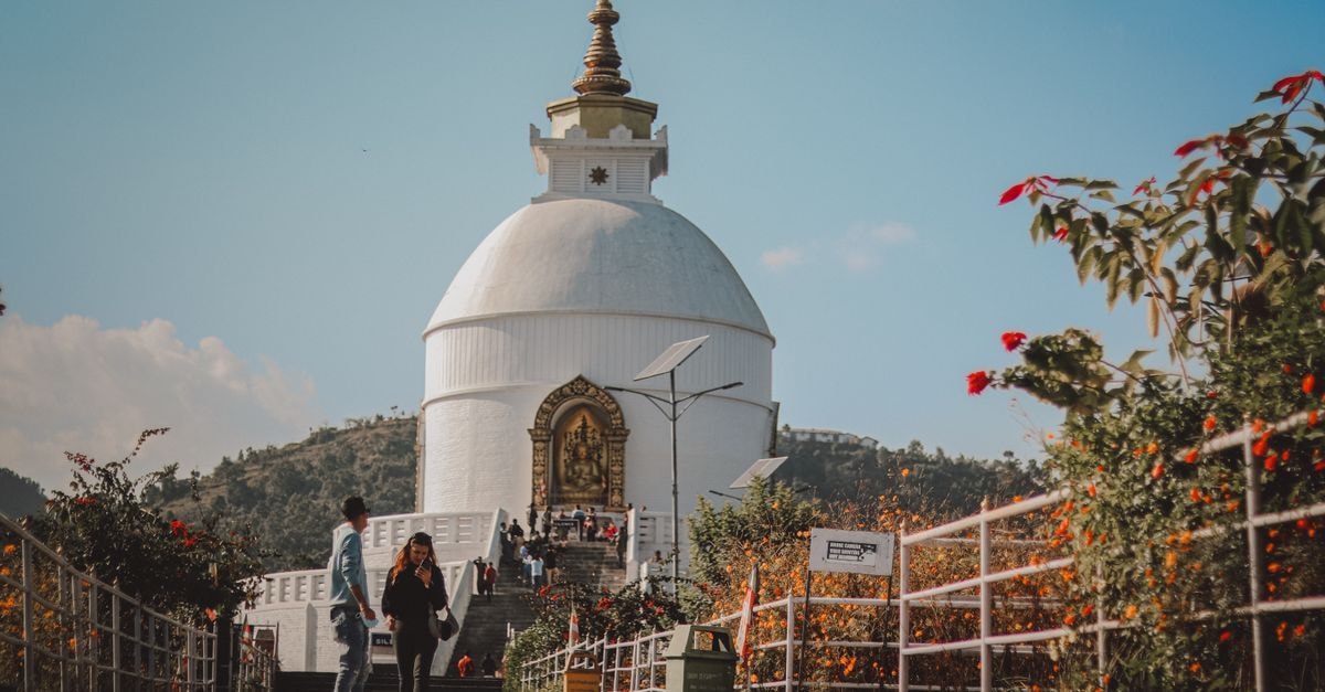 Tourists walking near the World Peace Pagoda surrounded by flowers in Nepal.
