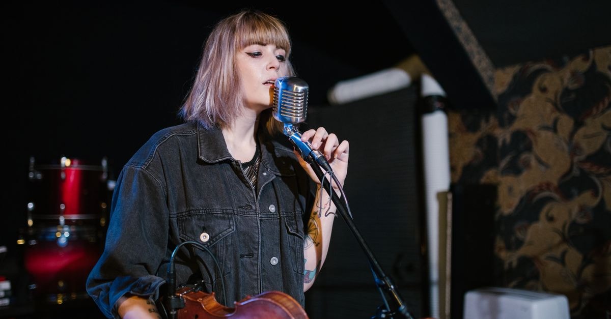Ella Langley〈Choosin' Texas〉以第 24 週稱霸 Hot 100 刷新紀錄 女子在舞臺上拿著小提琴對著復古麥克風唱歌。