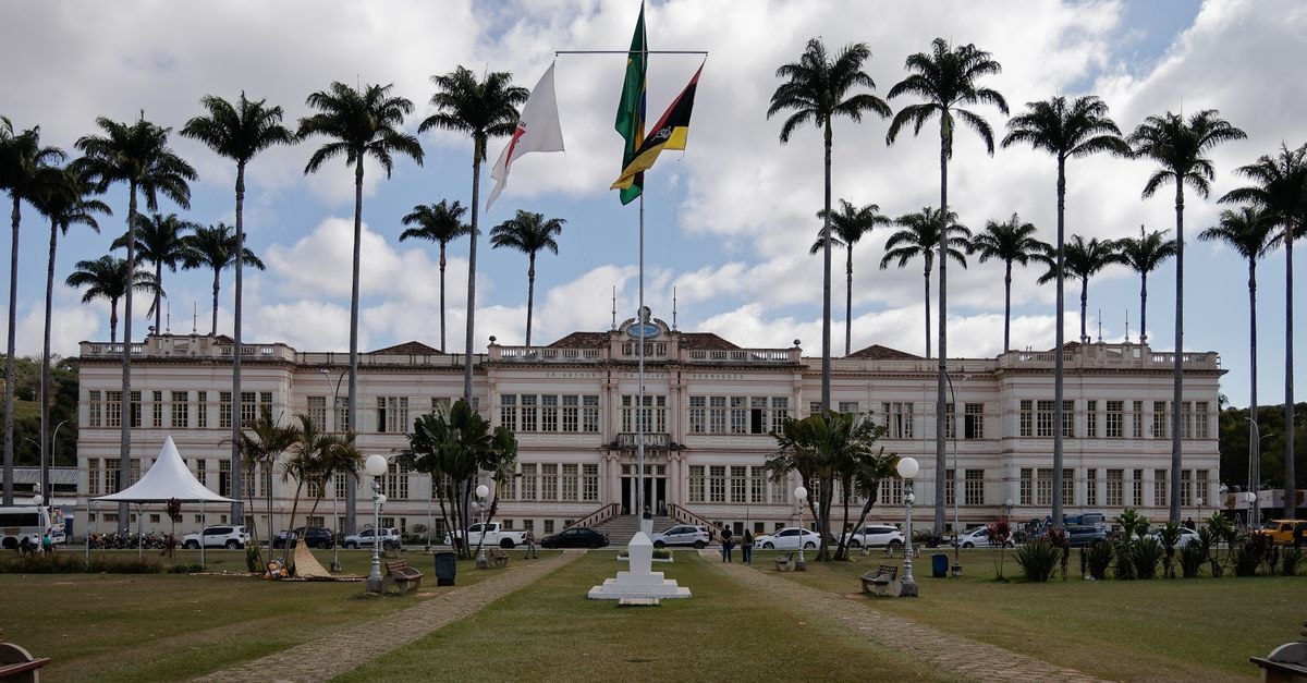 Patos de Minas Travel Guide: Culture, Food & City Ideas Elegant municipal building in Juiz de Fora, Brazil, surrounded by palm trees under a cloudy sky.