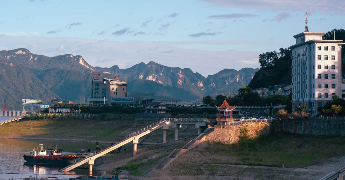 A Quiet Wonju Travel Guide: Paper Crafts, Bridges and Mountain Air Picturesque view of a riverside town featuring mountains, a pier, and a pagoda under a clear sky.
