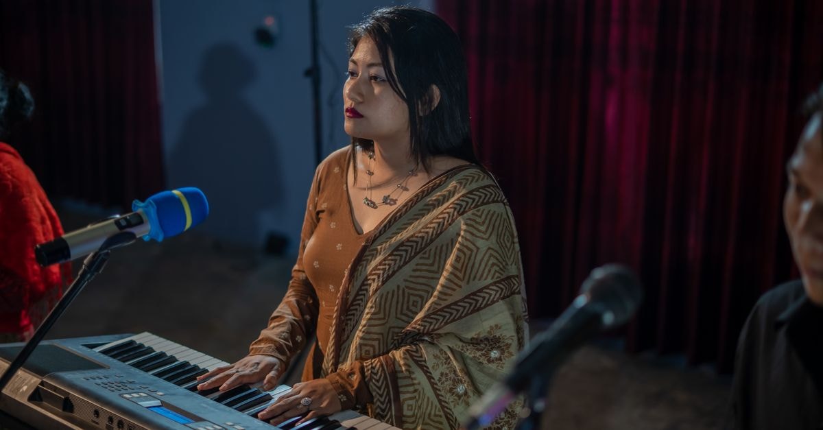Meesaya Murukku 2 opens in theaters with mixed early reviews praising music and Adhi's performance A woman playing a keyboard on stage with a microphone, wearing a saree.