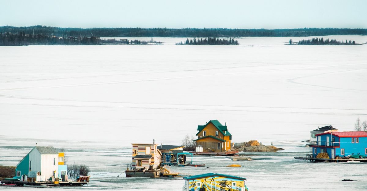 Yellowknife Travel Guide: A Calm Capital on the Edge of the North Vibrant houseboats on a serene frozen lake with a distant treeline, showcasing a unique winter landscape.