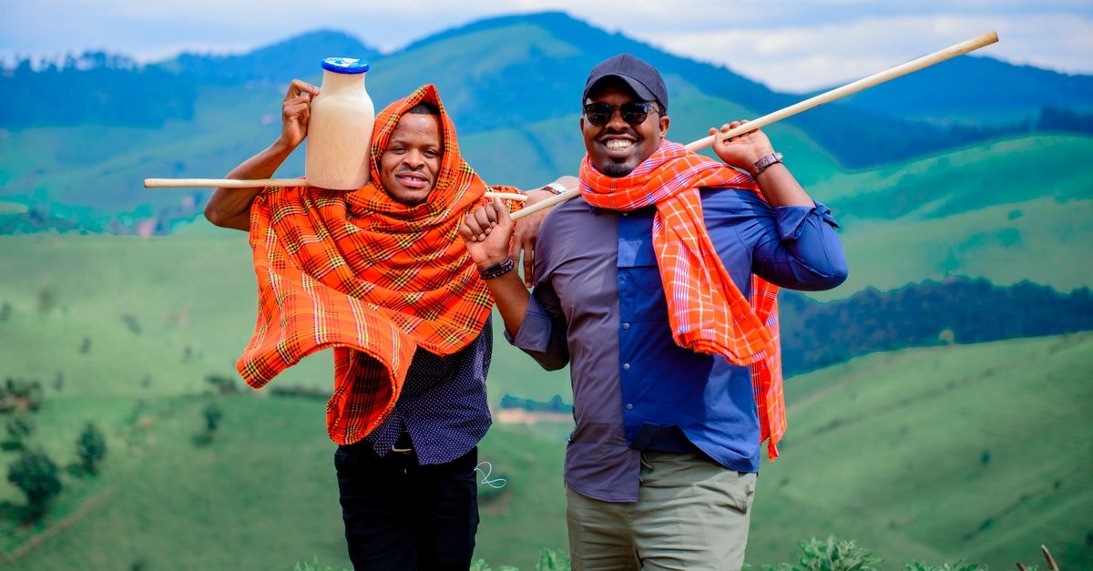 Mbeya Travel Guide: Southern Highlands Without the Rush Two men in colorful shawls smiling and posing with a milk jug in open green fields.