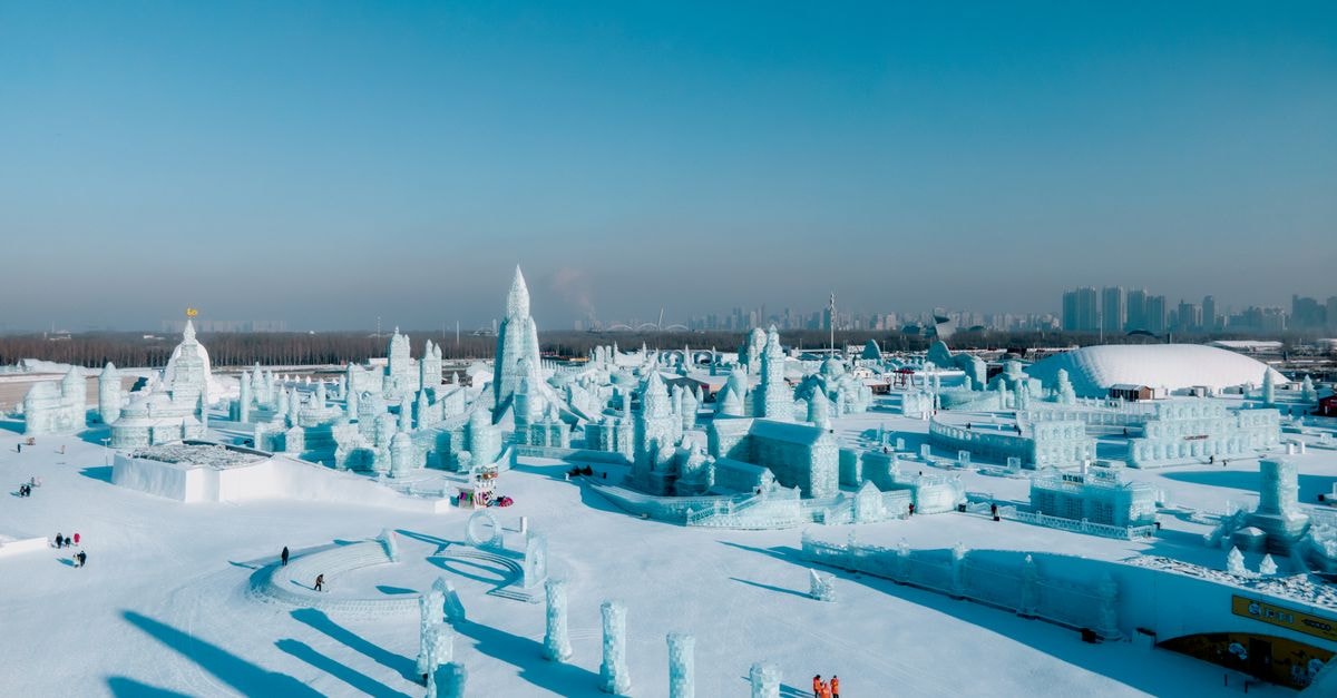 Stunning aerial view of Harbin Ice and Snow Festival with intricate ice sculptures under a clear blue sky.