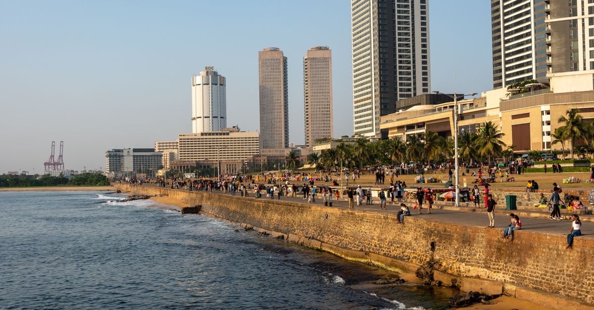 A bustling cityscape view of Colombo's Galle Face Green with people walking along the ocean in the evening light.