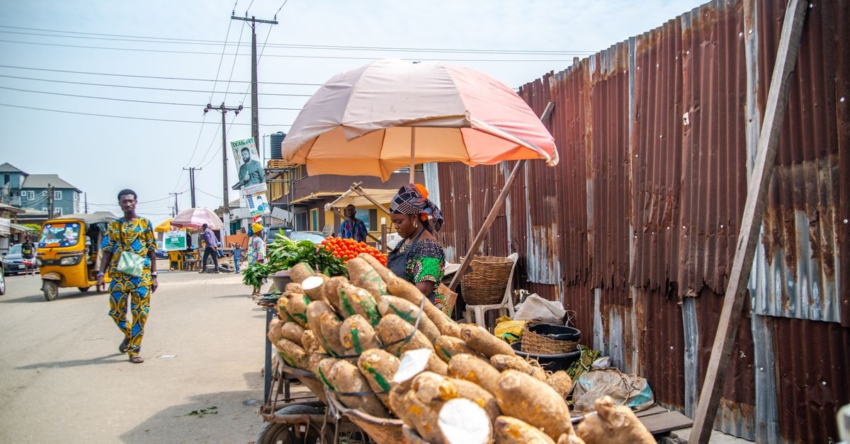 Colorful street market scene in Lagos, Nigeria, featuring a woman selling vegetables and yams.