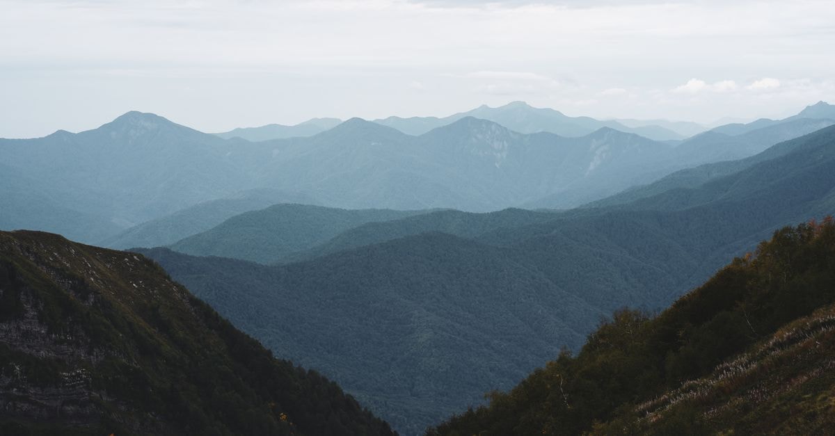 Capture the serene beauty of lush mountains under a soft blue sky in Sochi, Russia.