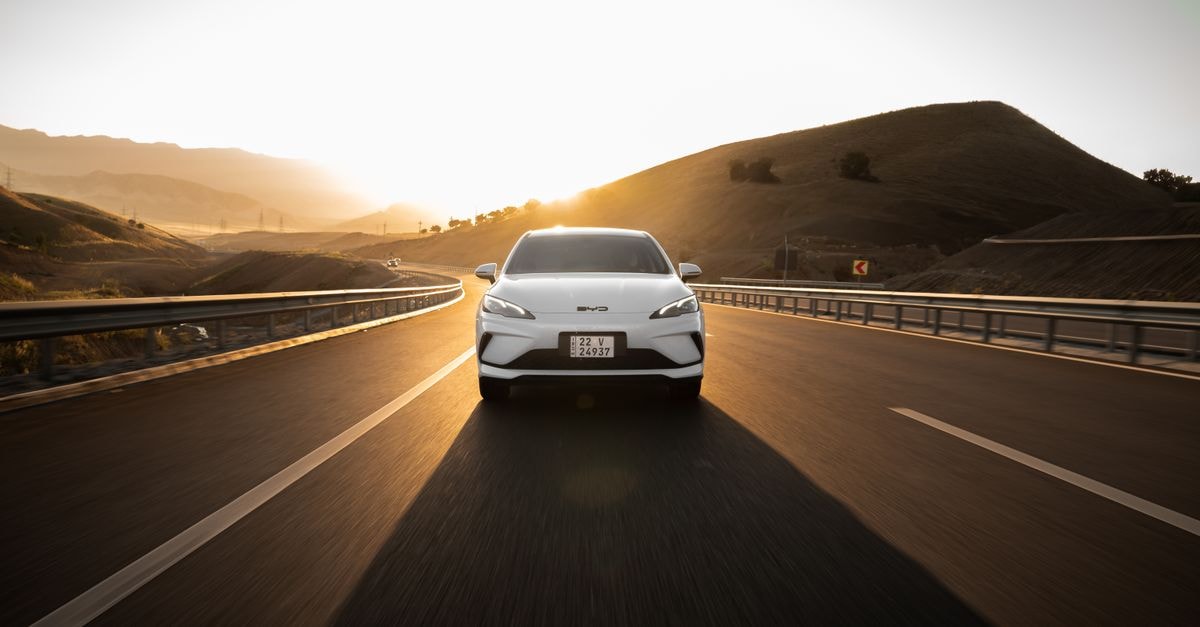 Foreign Carmakers Form 'Reverse Joint Ventures' With Chinese EV Partners Electric car driving on a scenic highway at sunset, highlighting modern automotive design and sustainable travel.