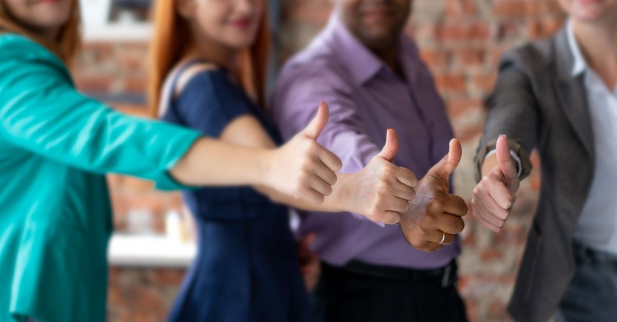 Unrecognizable cheerful colleagues in formal clothes showing thumbs up gesture while standing in modern office during teamwork on blurred background