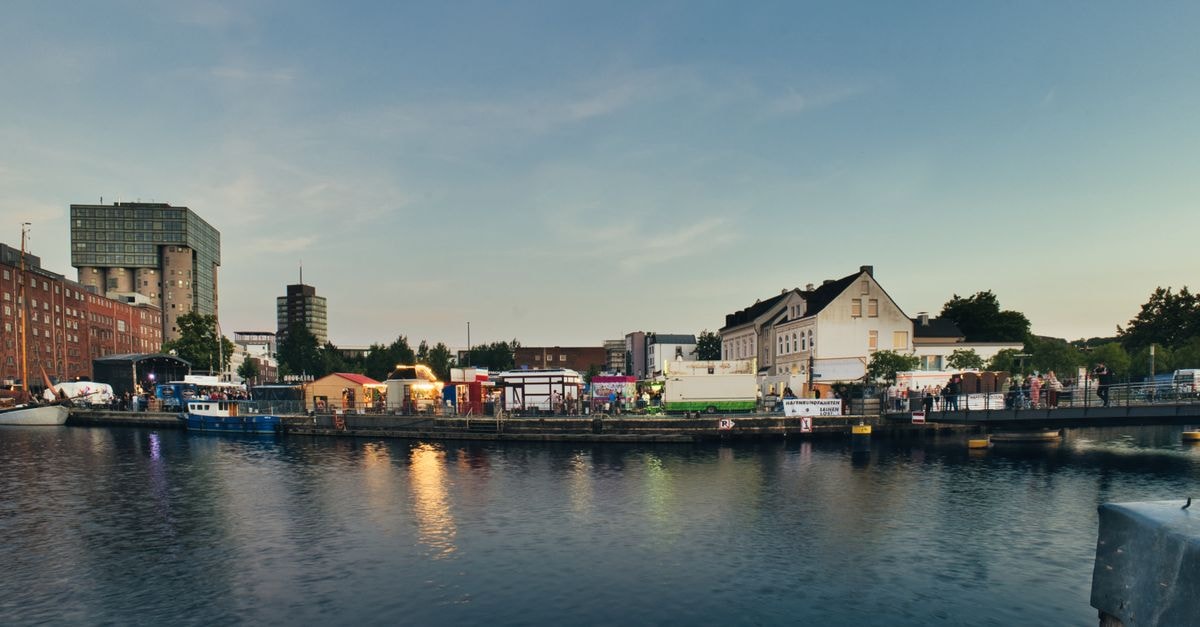 Kiel travel guide: ferries, buses, and fjord views Evening view of a lively urban harbor with buildings and calm water reflections.