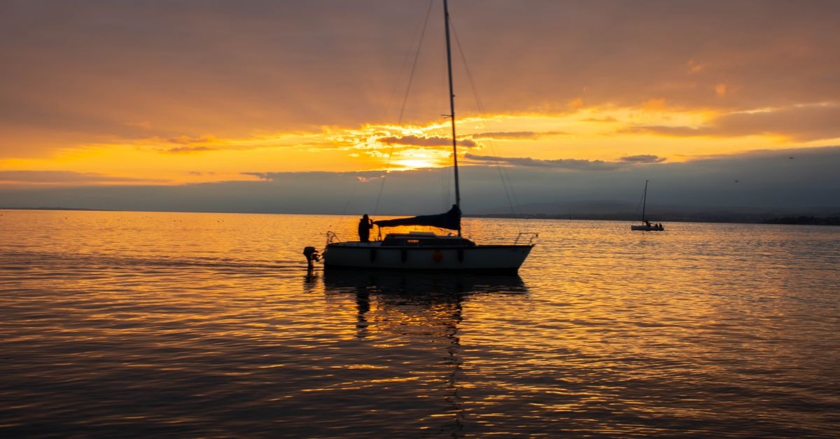 A Slow Travel Guide to Lausanne: Lakeside Charm A peaceful sunset scene with a sailboat silhouetted against the golden horizon on Lake Lausanne.
