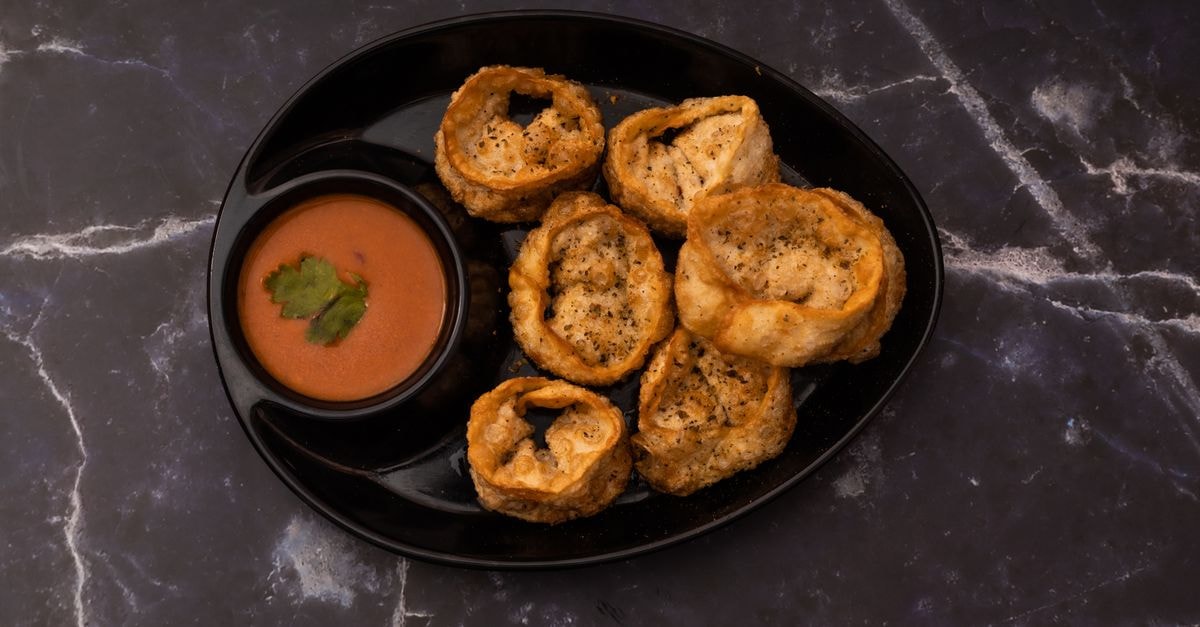 Super Hotel O Gorakhpur Industrial Area in Gorakhpur: A Practical Stay in the Industrial Hub Delicious crispy cheese corn momos served with a spicy dipping sauce on a black plate.