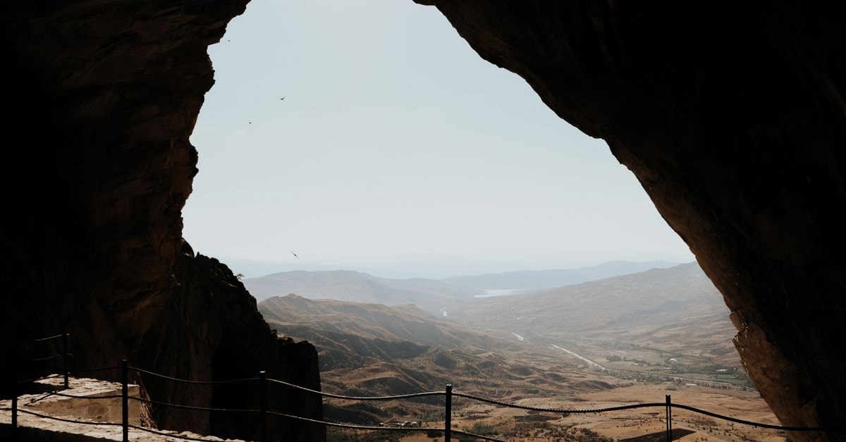 View from a large cave opening overlooking wide, sunlit valleys and distant mountains.