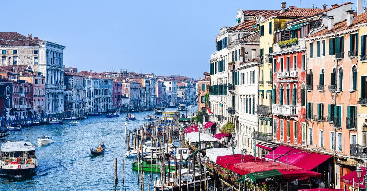 WellVenice Grand Canal: Spacious San Polo Apartment Overlooking the Lagoon Scenic view of Venice's Grand Canal with colorful buildings and gondolas under a clear sky.