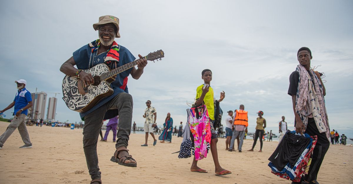 A lively street musician captivates a crowd with his guitar on a bustling beach.