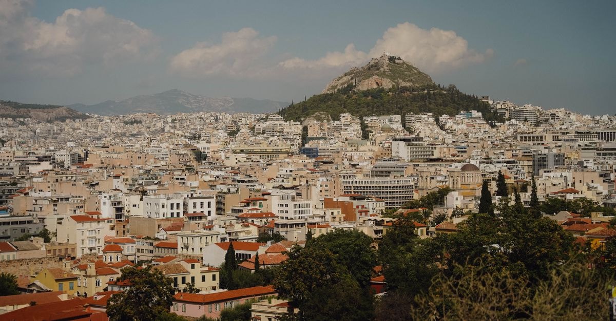 New Hotel Athens: A Design-Led Reinvention in Syntagma A stunning view of Athens cityscape with iconic Lycabettus Hill under a partly cloudy sky.
