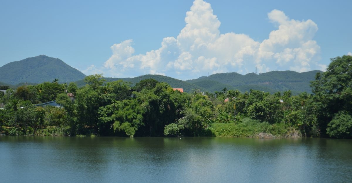 A tranquil lake scene with lush greenery and mountains under a bright blue sky.