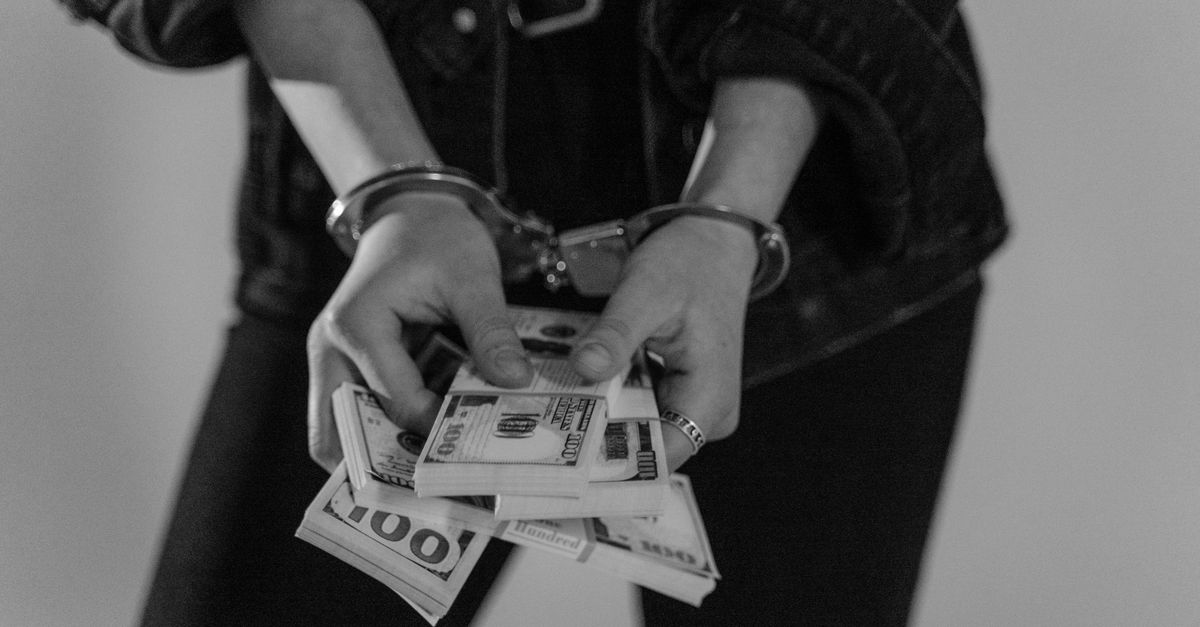 Black and white image of a handcuffed person holding bundles of US dollars.