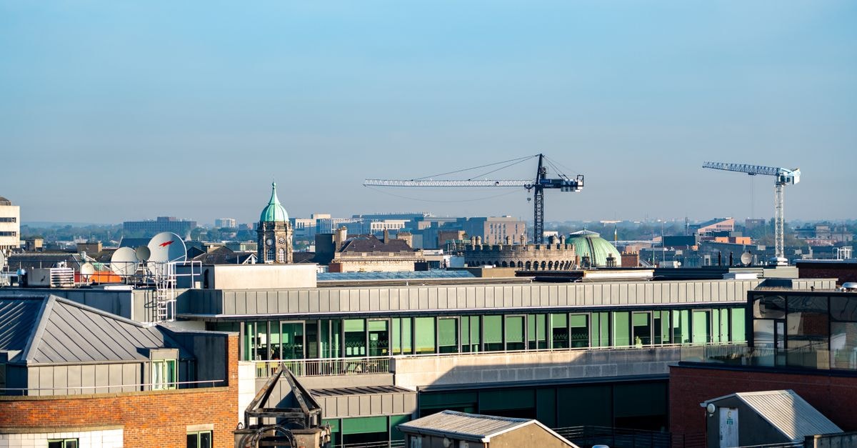 A vibrant view of Dublin's cityscape featuring construction cranes and iconic architecture under a clear blue sky.