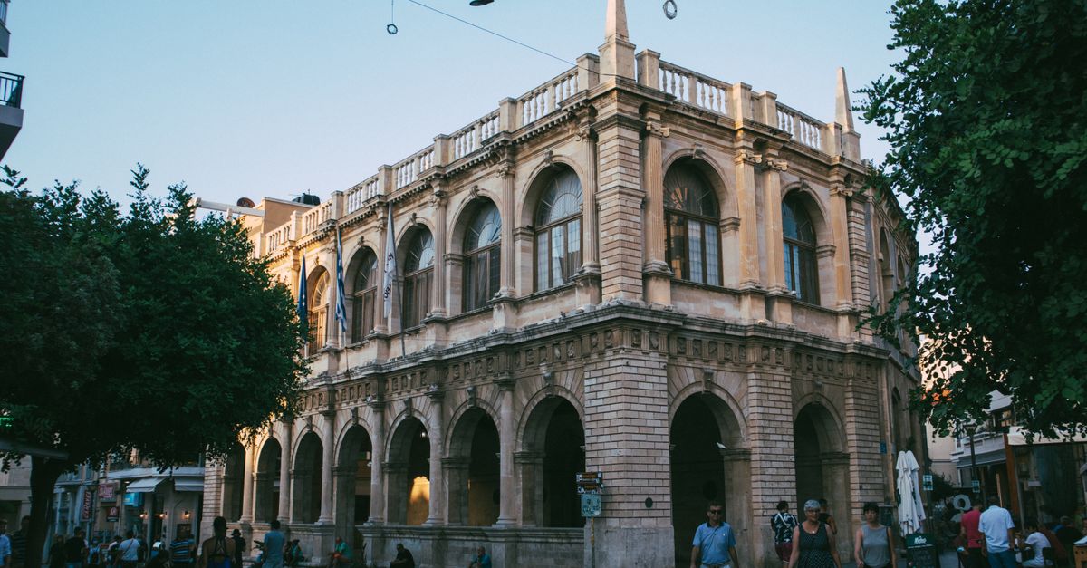 A picturesque historic building in a European town square captured at dusk, with people strolling nearby.