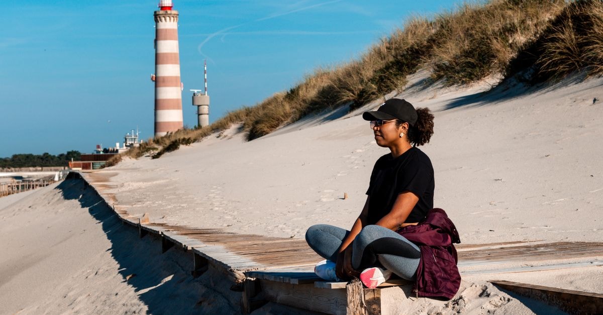 Aveiro travel guide: canals, moliceiros and slow coastal charm Woman meditating near Aveiro's iconic lighthouse in a tranquil beach setting.