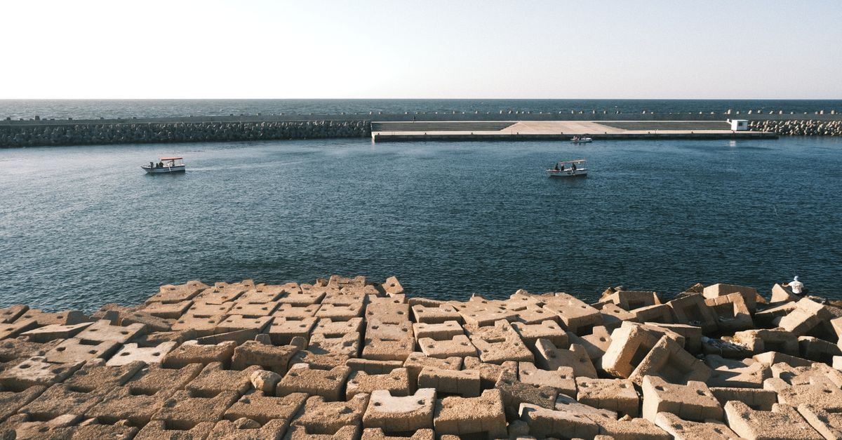 Tranquil scene of boats near a stone breakwater in Alexandria harbor under a clear sky.