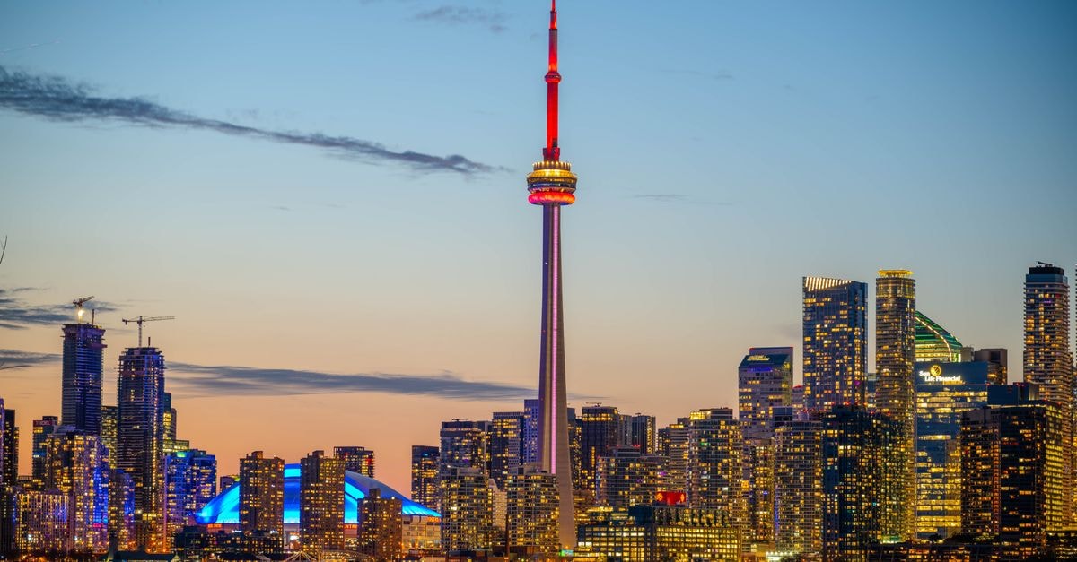 Beautiful sunset view of Toronto skyline with CN Tower and city lights reflecting on the lake.