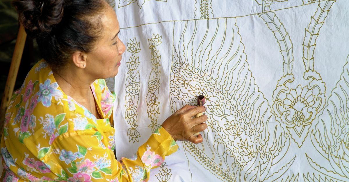 Pekalongan Travel Guide: Batik Heritage and Home Cooking Craftswoman making intricate batik patterns on fabric in West Java, Indonesia.
