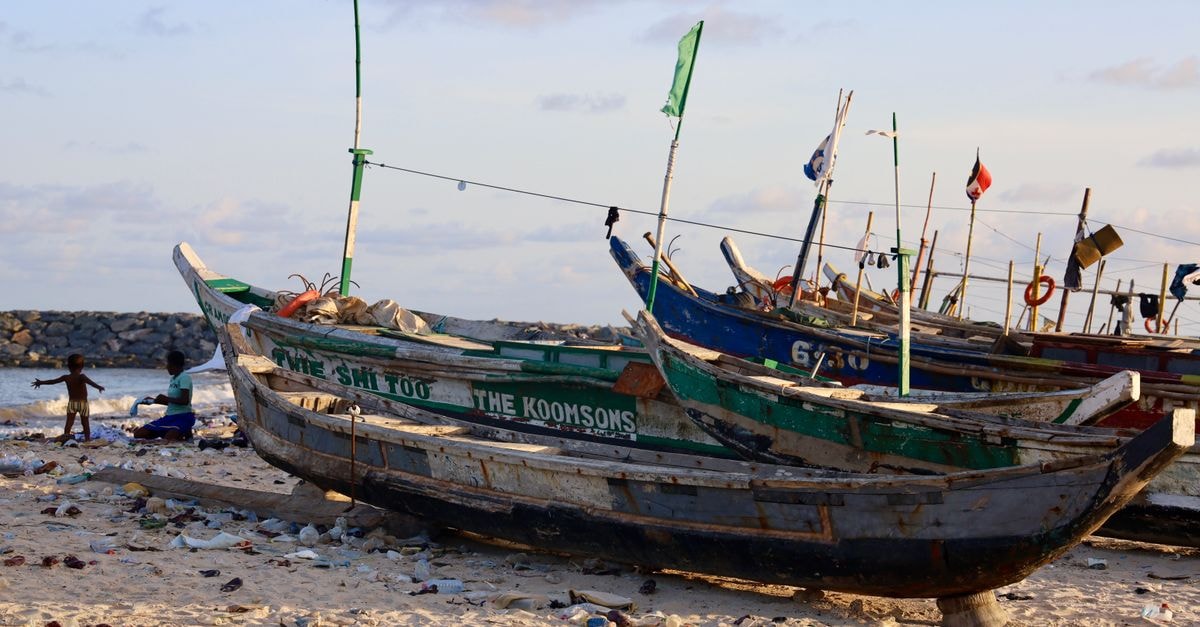 An Accra Travel Guide: Markets, History and Everyday Ghana Wooden fishing boats rest on a littered beach in Accra, Ghana, with children playing nearby at sunset.