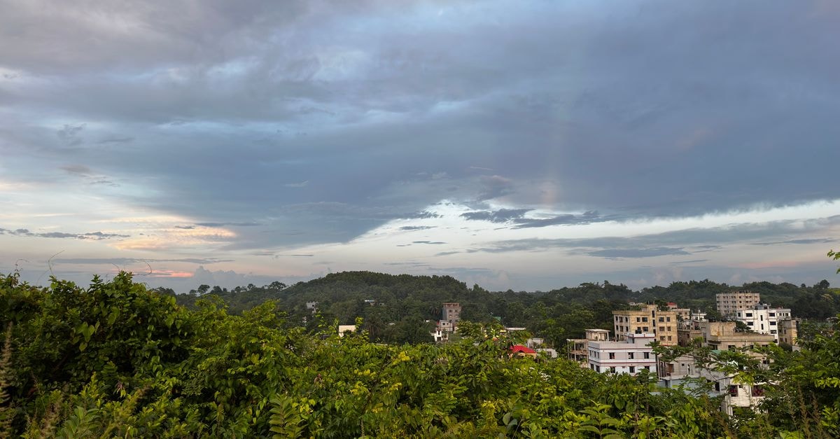Mahabir Guest House, Siliguri — Central Stay Since 1985 A picturesque view of a small urban area surrounded by lush greenery under a cloudy sky.
