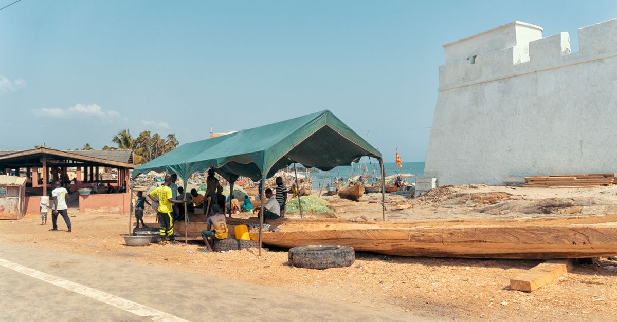 Market scene under a green tent near Elmina Castle, Ghana. People gathered by the seaside.