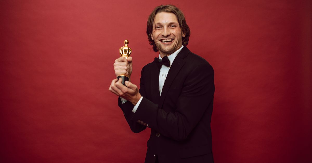 Ryan Coogler takes best original screenplay Oscar for Sinners as Indian designers light up the red carpet Smiling man in a tuxedo holding a trophy against a red background, celebrating success.