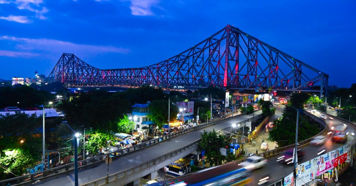 Vibrant evening view of Howrah Bridge in Kolkata with dynamic traffic and city lights.