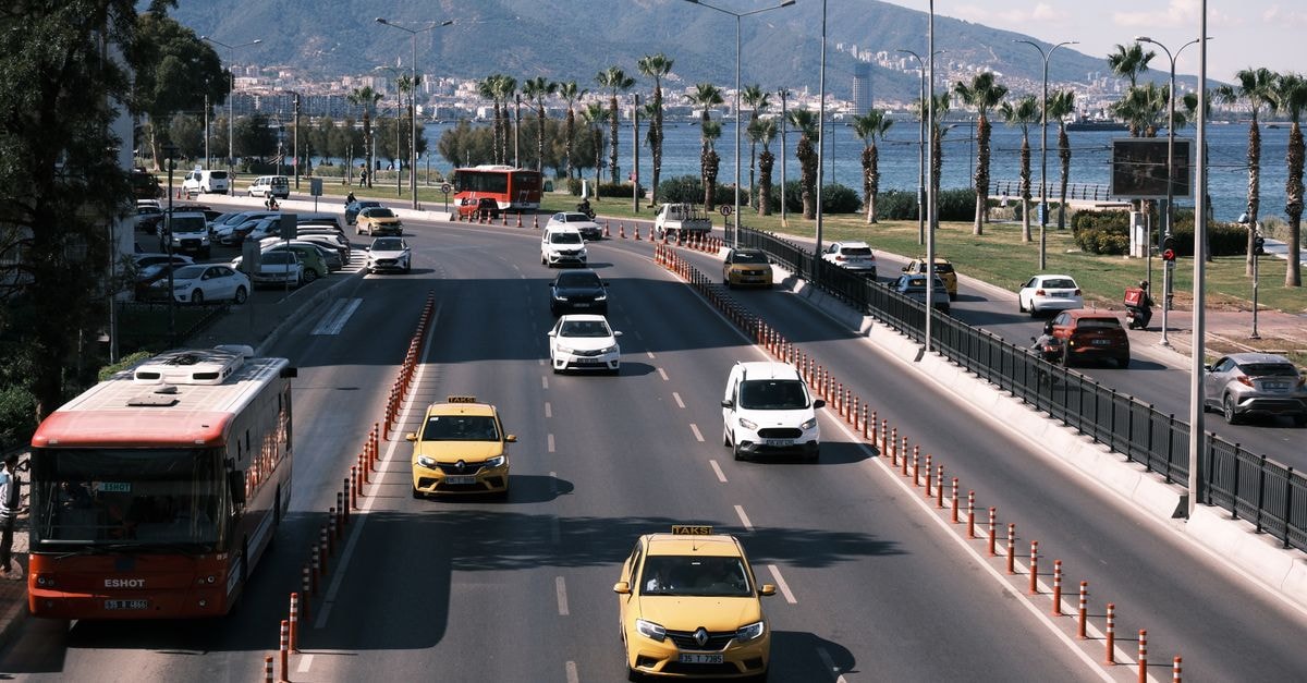 Renaissance Izmir Hotel in Izmir: Kordon-Adjacent Stay with Turkish Bath Bright daytime traffic on a coastal road in İzmir, showcasing a scenic view with palm trees and mountains.