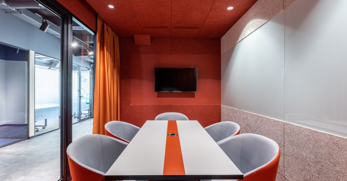 Comfortable chairs at tale placed against red wall with TV in modern conference room with glass wall in business center
