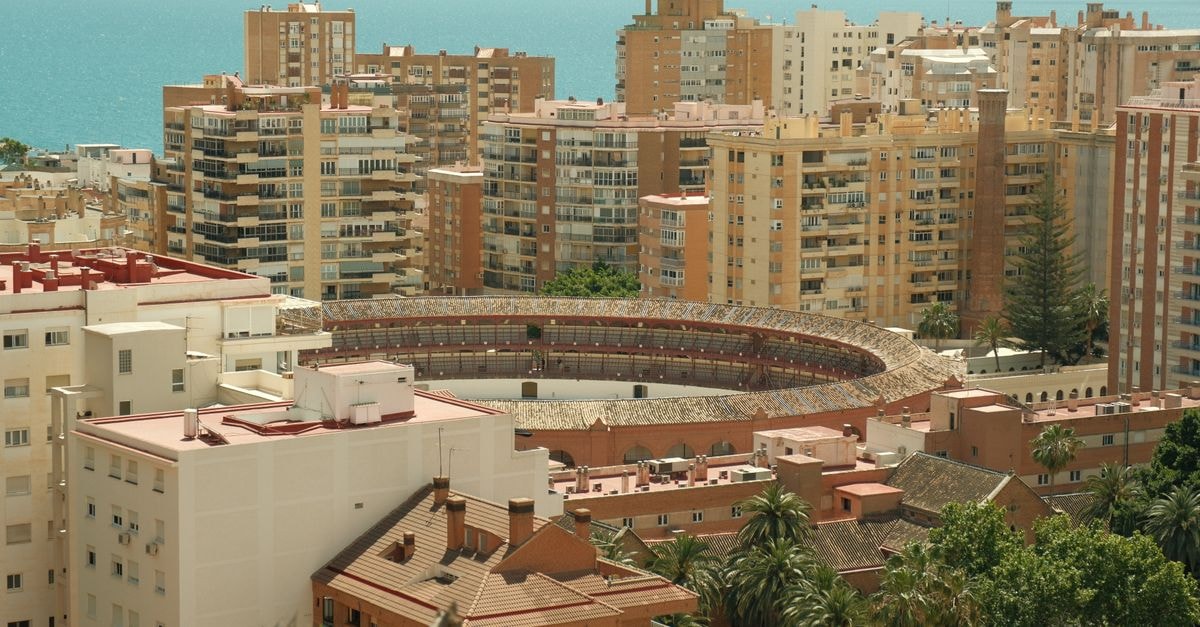 Stunning aerial shot of Malaga's bullring surrounded by modern buildings and the Mediterranean Sea.