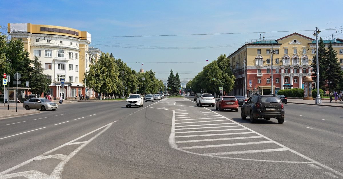 A bustling urban street scene with cars, trees, and historic buildings under a clear sky.