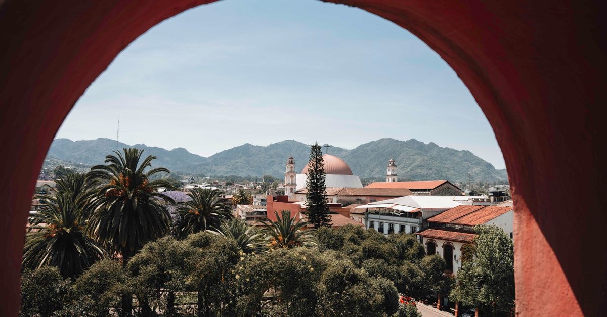 Hostal El Bunker in Tumbes: Avenida Castilla Stop with Local Hostal Vibe Beautiful view of Huauchinango's architecture through an arch, featuring domed churches and lush greenery.