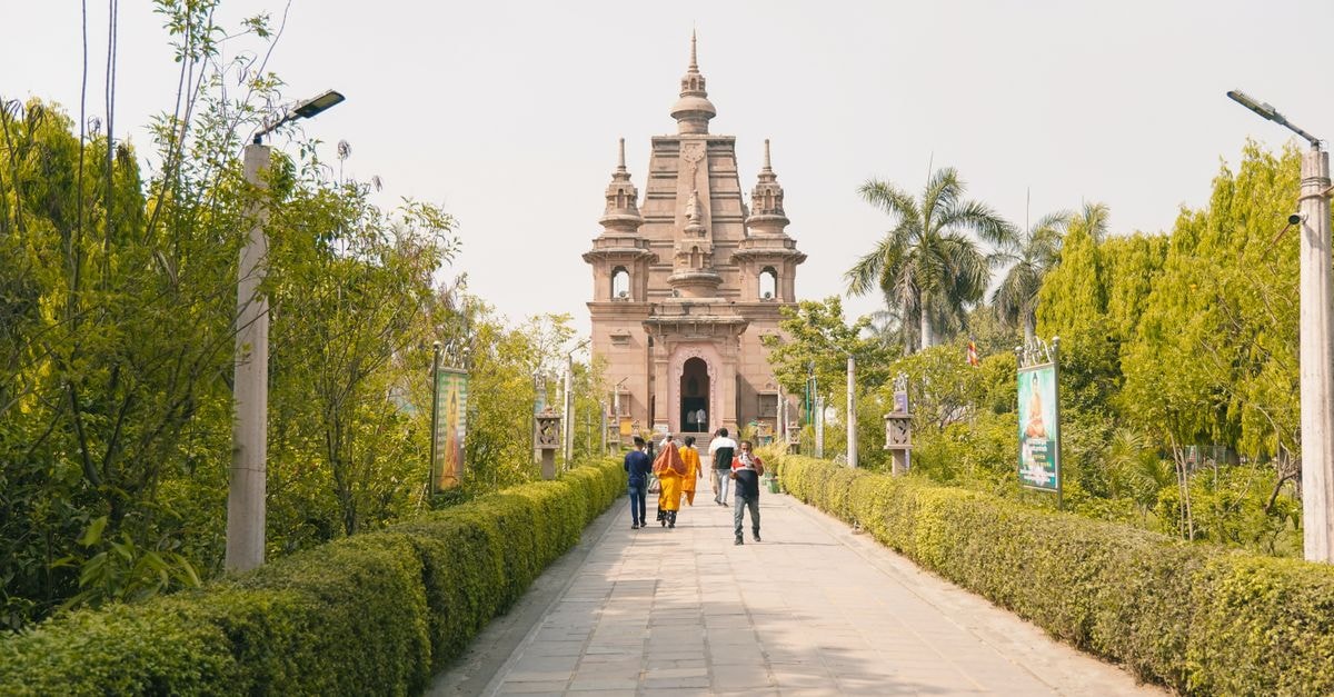 People walking on a garden pathway towards an ancient temple with lush greenery.