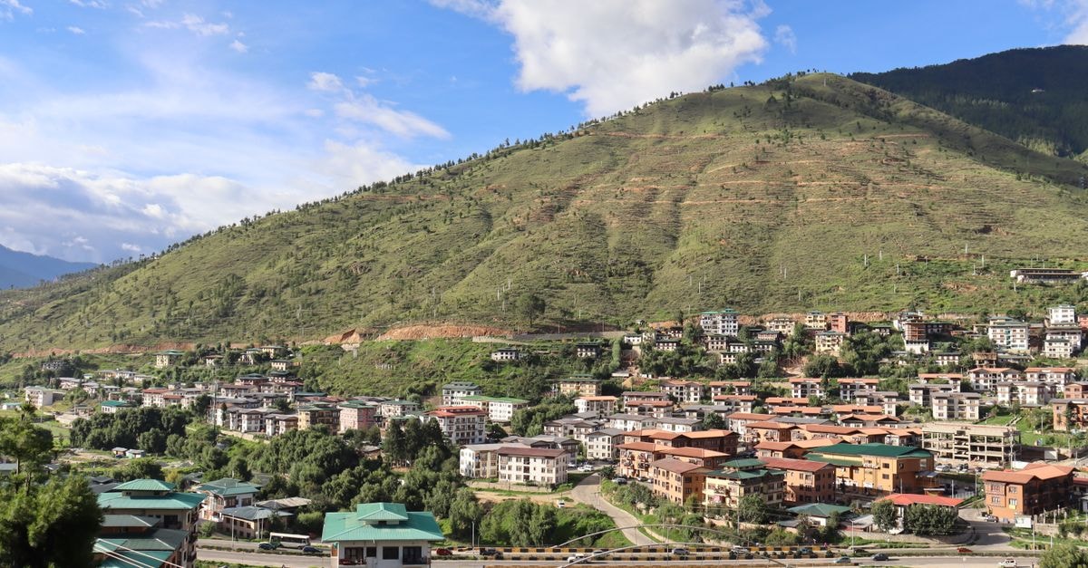 Thimphu travel guide: slow days in Bhutan's mountain capital A picturesque view of a mountain town featuring a bridge and residential buildings.