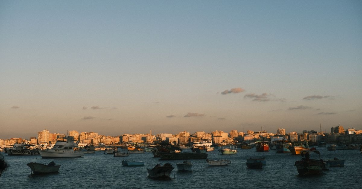 Tripoli travel guide: a slow Mediterranean evening by the corniche A serene view of boats in Alexandria's coastal harbor during sunset with city skyline.