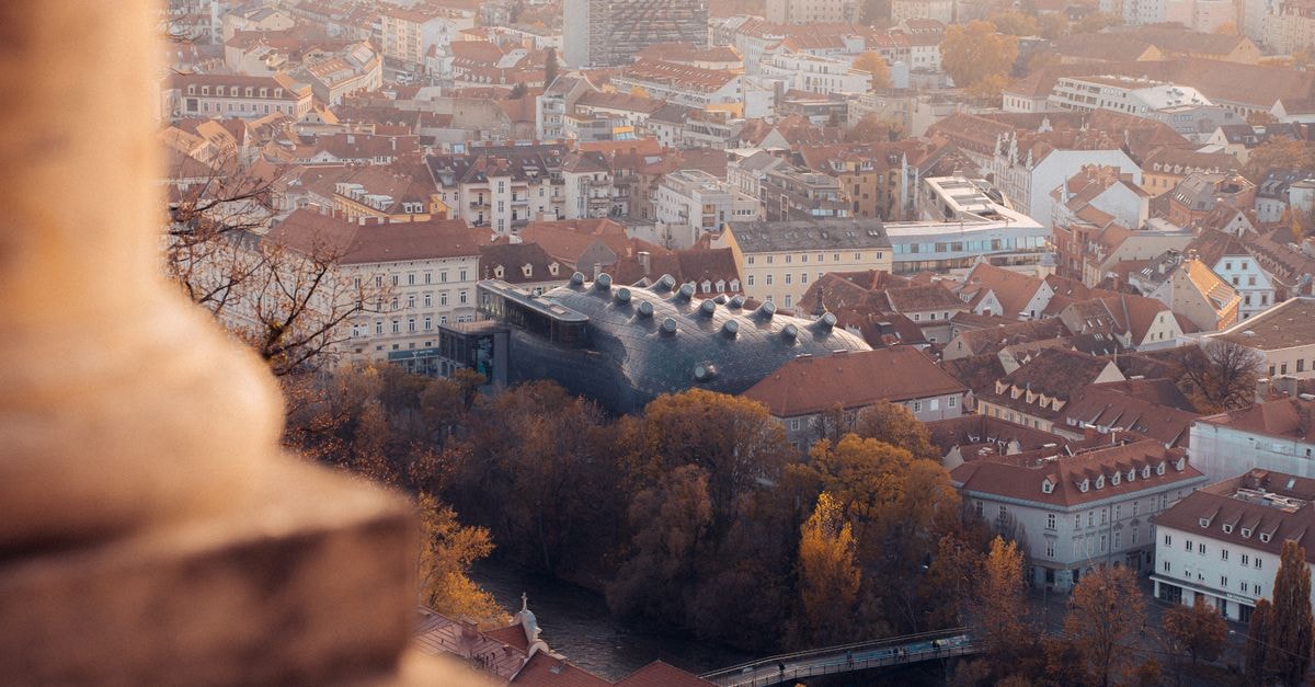Hotel Mariahilf, Graz — A Heritage Stay by the Kunsthaus Stunning aerial view of Graz cityscape featuring the unique Kunsthaus Graz building amid autumn colors.