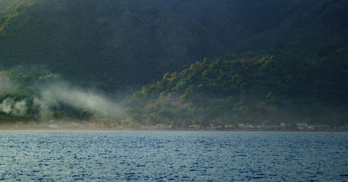 Nacaome Travel Guide: A Slow Look at Southern Honduras Tranquil view of a coastal village nestled against a lush mountain with mist rising at sunset.